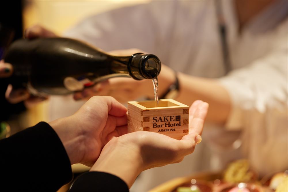 SAKE Bar Hotel 浅草。チェックインをしたら到着の印しに枡をお受け取り下さい。館内を巡る際は日本酒『雨降』シリーズの研ぎ澄まされた個々の酒質を飲み比べてお楽しみください。